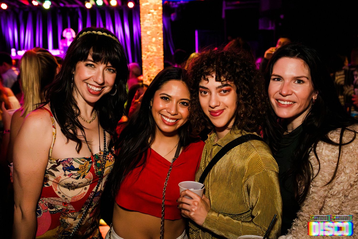 Friends smile together at a nightclub with purple lighting and festive atmosphere.