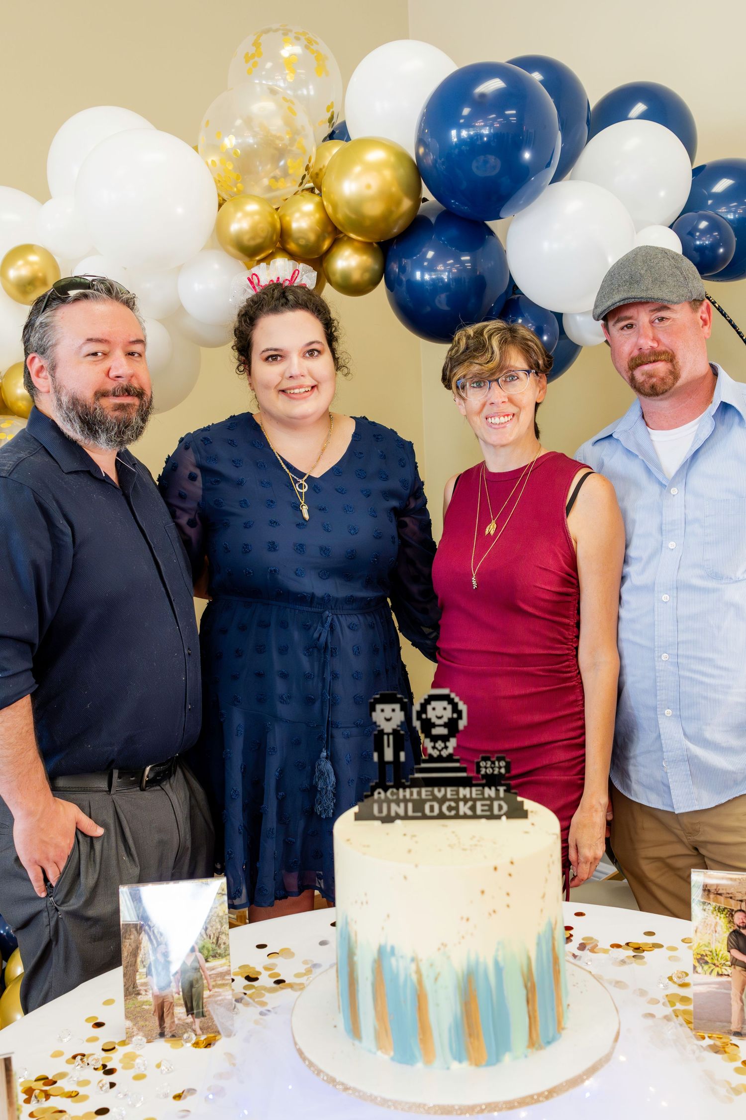 A celebration with a blue and gold balloon arch backdrop and a decorated cake featuring small trophy toppers.