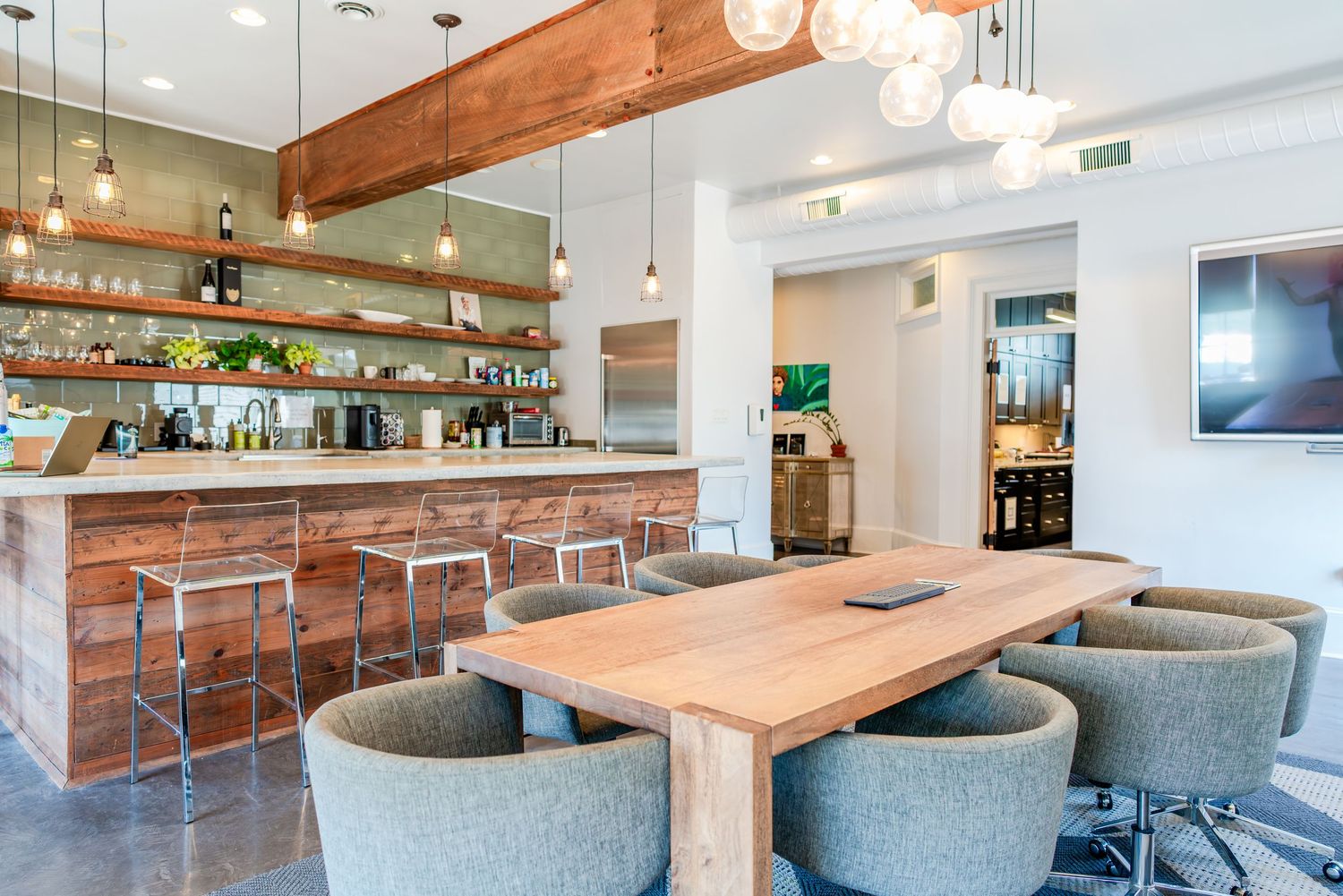 Modern restaurant interior with wooden bar counter, gray upholstered chairs, and pendant lighting in airy white space.