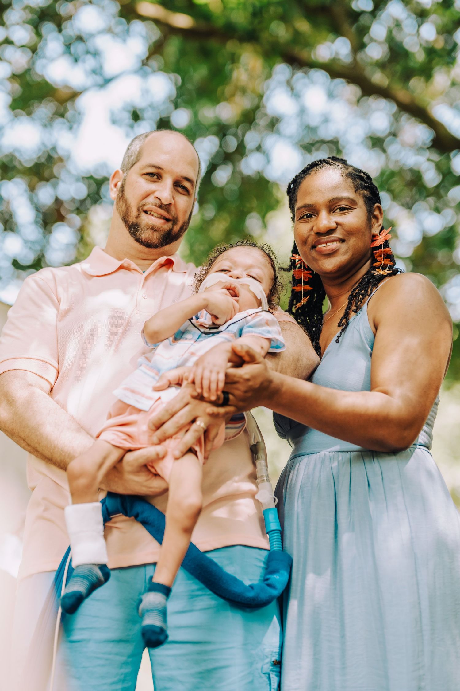 Family of three smiling together outdoors on a sunny day wearing coordinated pastel outfits.