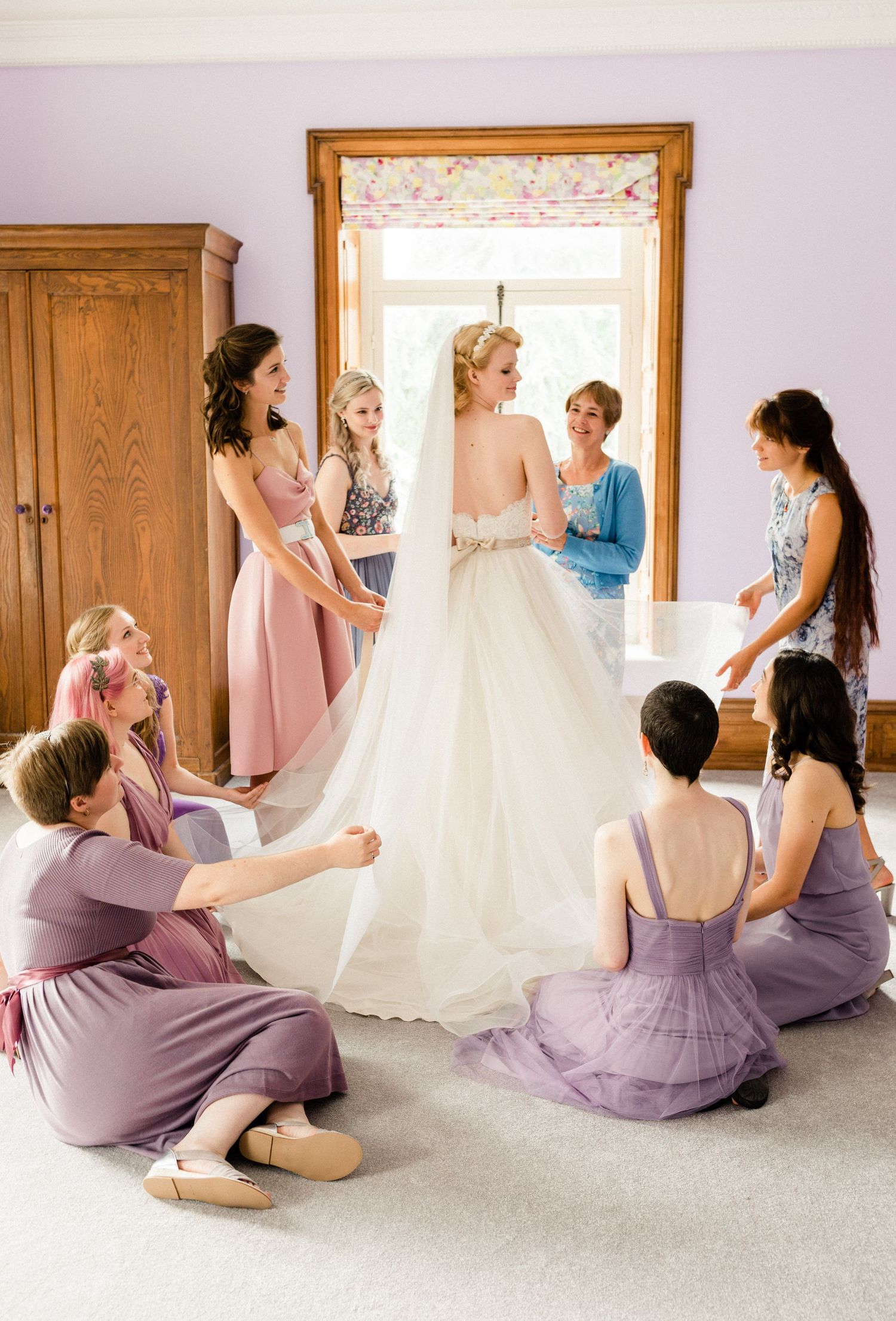 Candid bridal preparation bridesmaids assisting with dress and veil