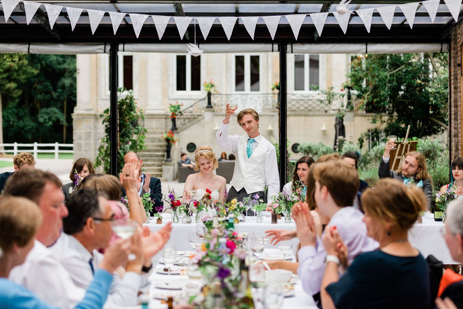 Documentary-style image of groom raising glass in wedding reception in France