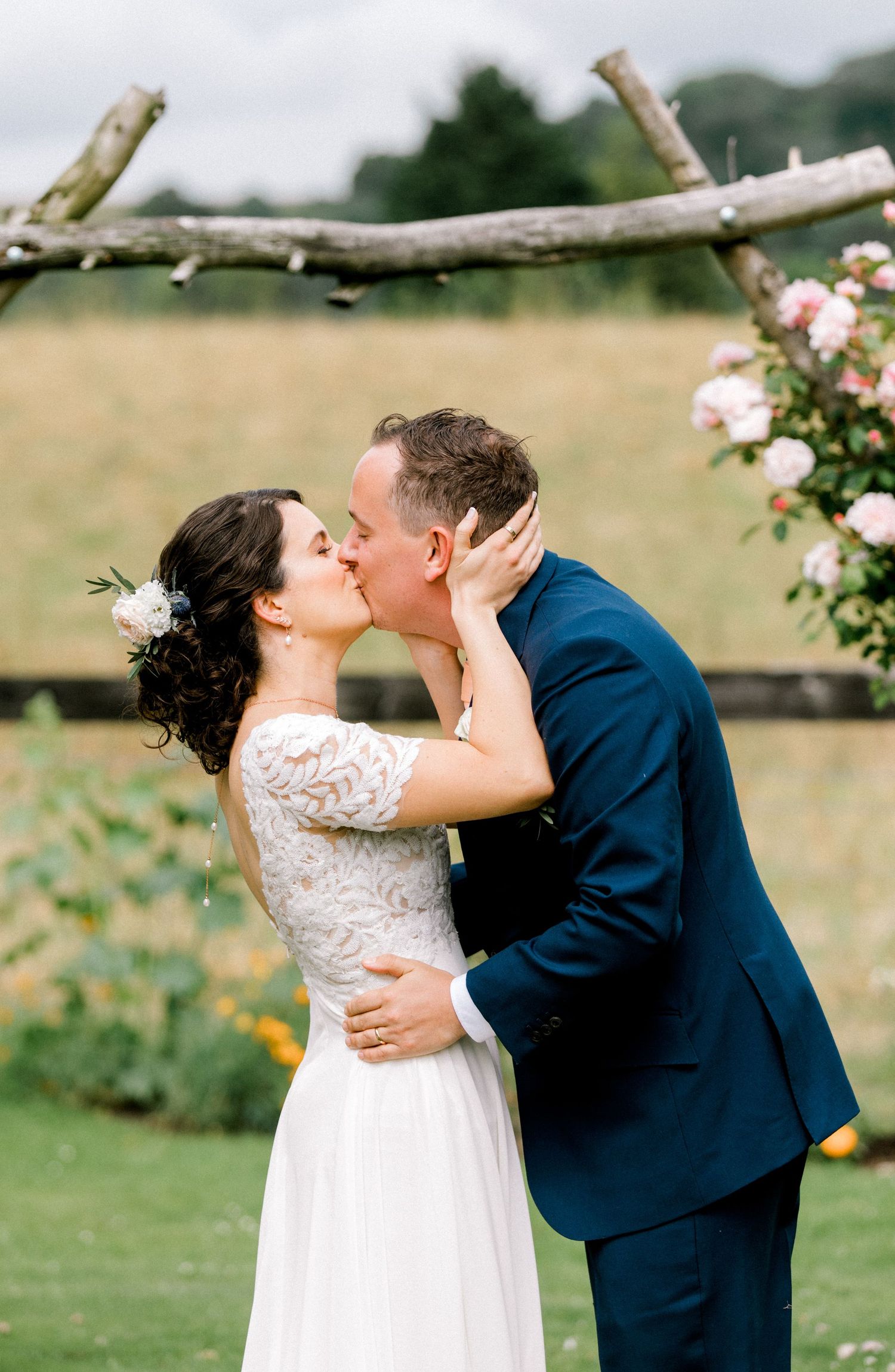 Candid moment of newlyweds kissing under floral arch at countryside ceremony London