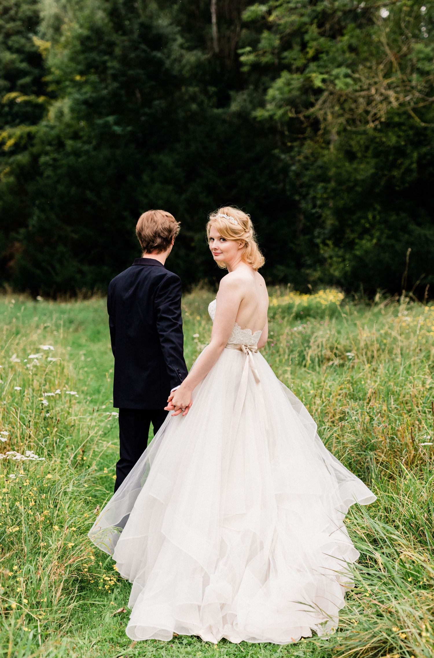 Romantic wedding photography showing groom guiding bride as she glances back toward photographer