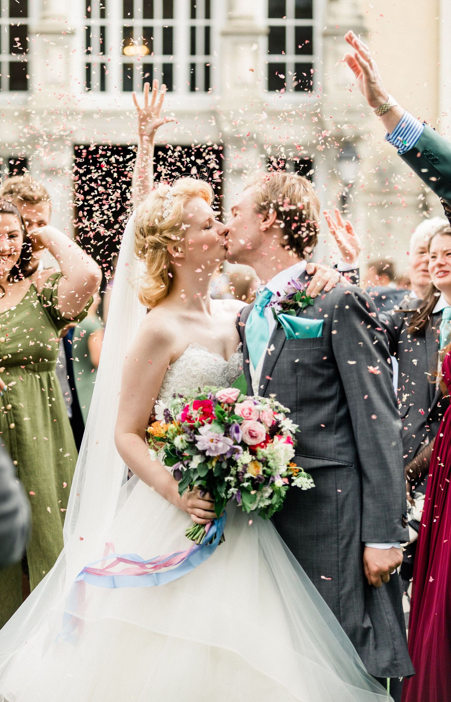 Bride and groom kissing under colourful confetti shower during wedding celebration