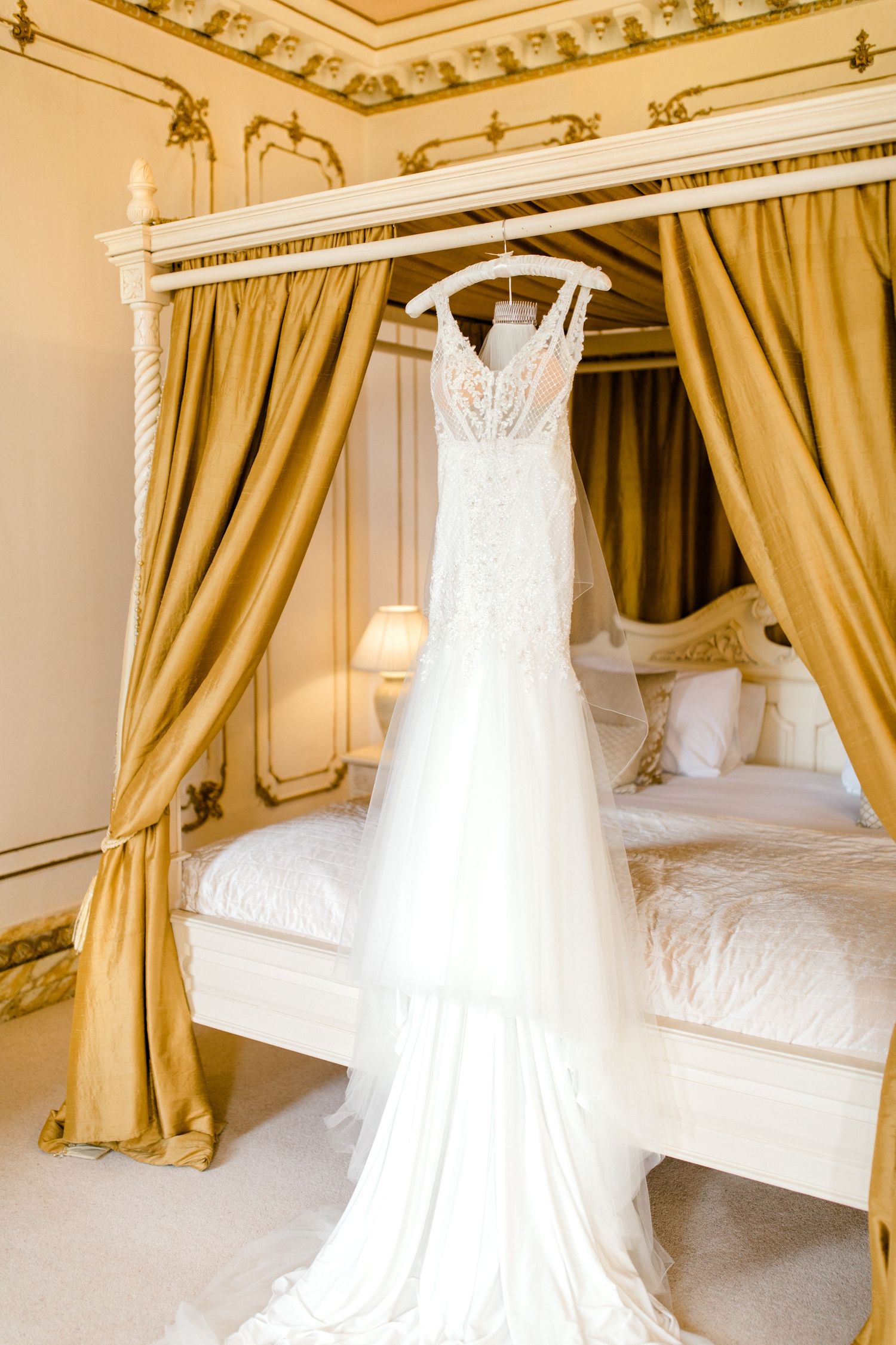 Lace wedding gown suspended in soft window light – romantic bridal prep at a manor house Gosfield Hall Essex - candid wedding photography