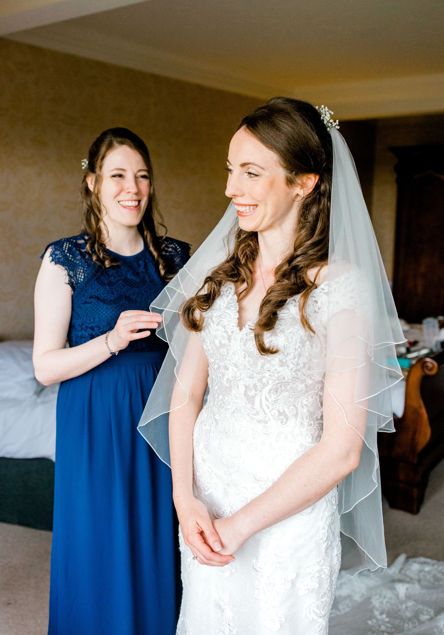 Sister and maid of honour helping with the veil in soft window light – natural light bridal prep. Hoath House, Edenbridge Kent