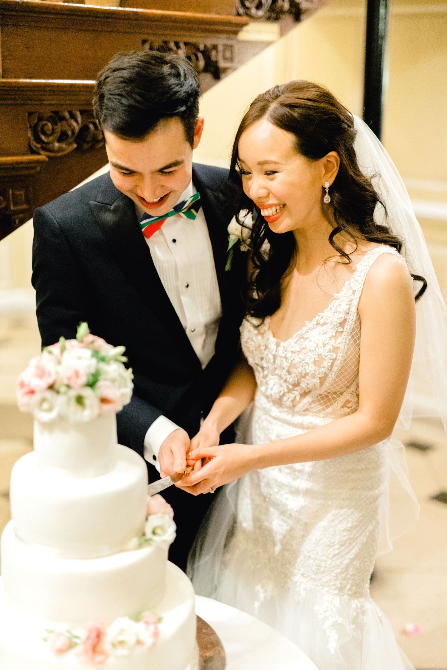 Newlyweds laughing as they slice into a three-tier buttercream cake – candid cake cutting photo Gosfield Hall Essex
