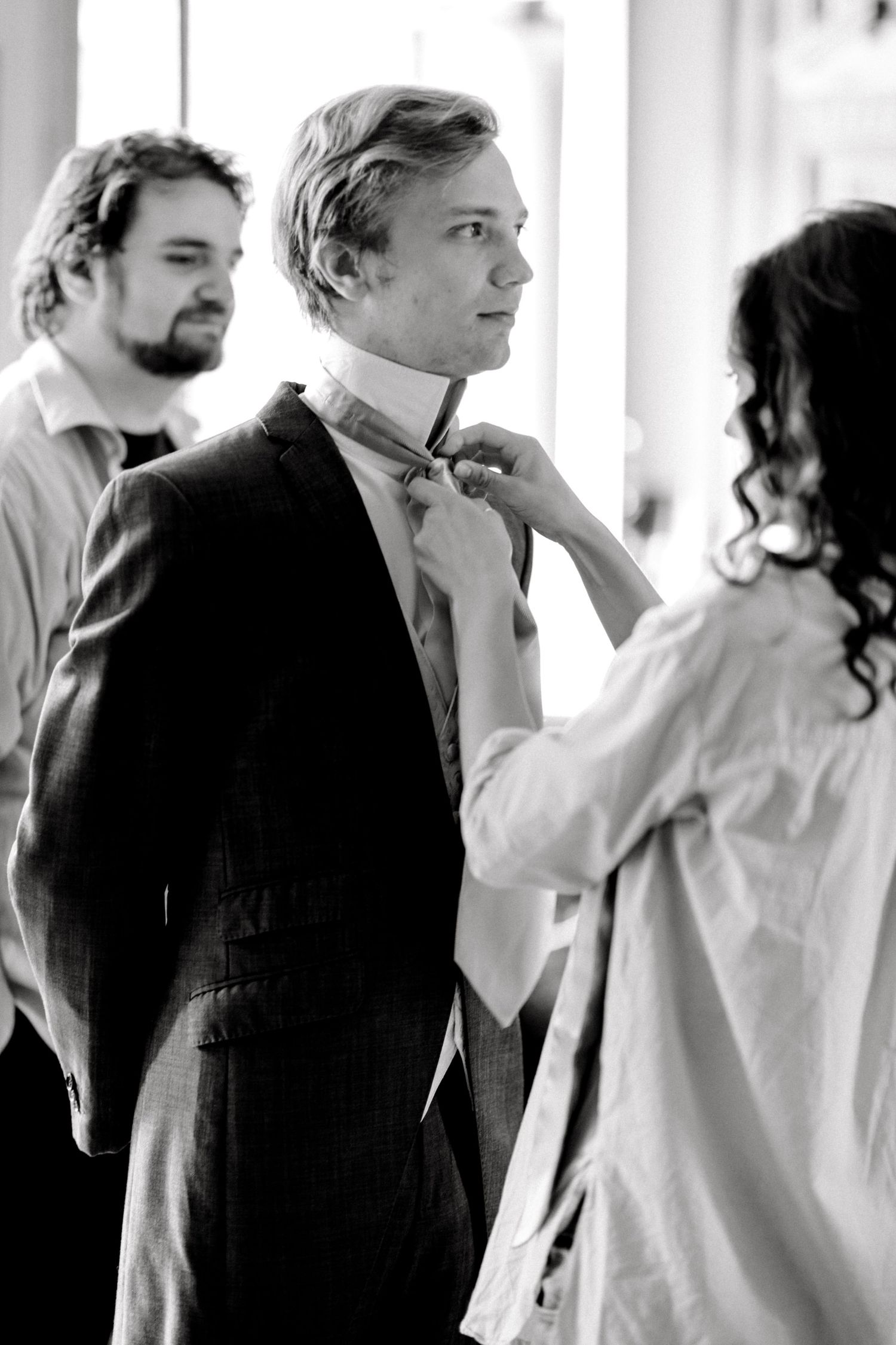 Candid moment of groomsmen fixing groom's tie during morning prep at London venue