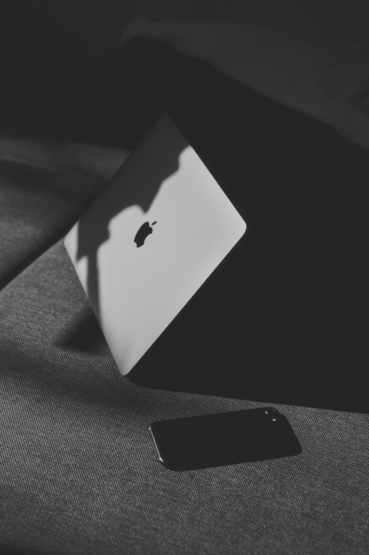 Black and white image of a MacBook laptop and smartphone on a textured surface helping with Senior Banners and Sports Photography.
