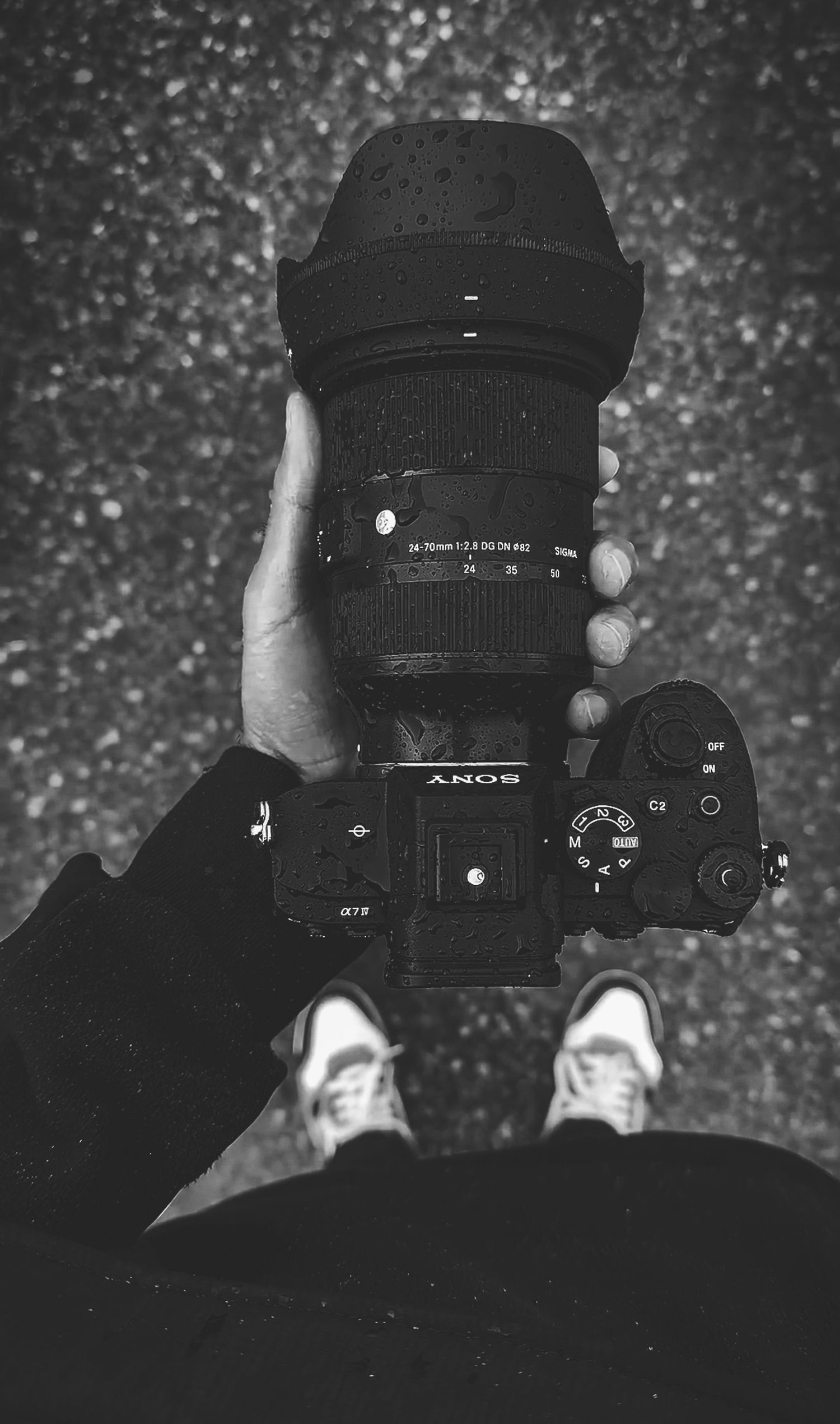 Black and white photo of hands holding Sony camera with large lens against textured ground helping with All Photography