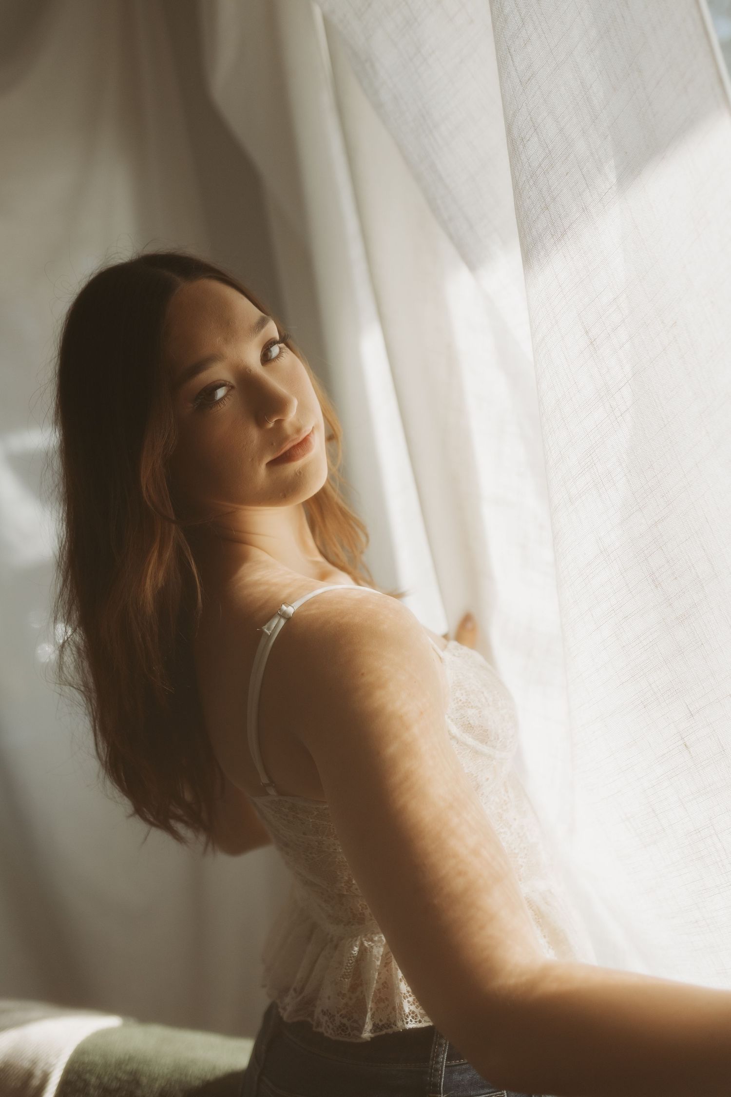 A dreamy boudoir photoshoot with soft white curtains and natural light creating an ethereal atmosphere.