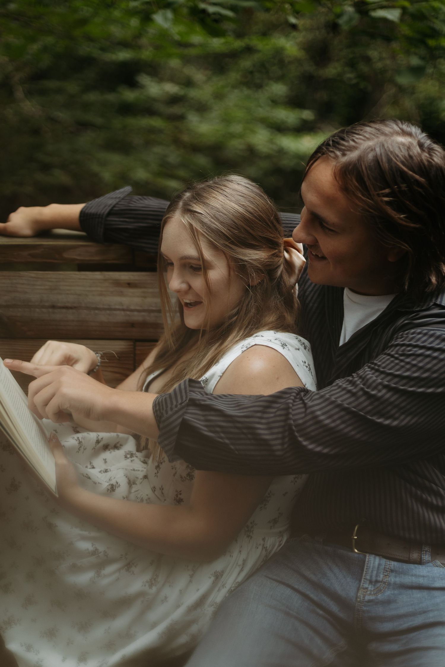 A young couple shares a romantic moment reading a book together outdoors near a wooden structure.