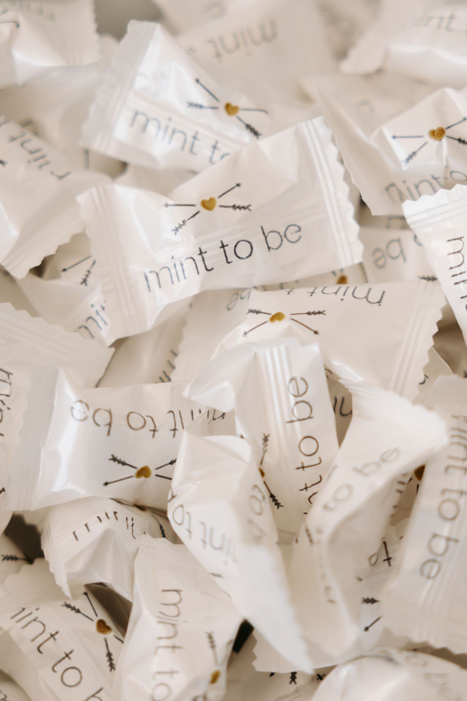 Wedding favor mints in white wrappers printed with mint to be phrase and arrow heart design.