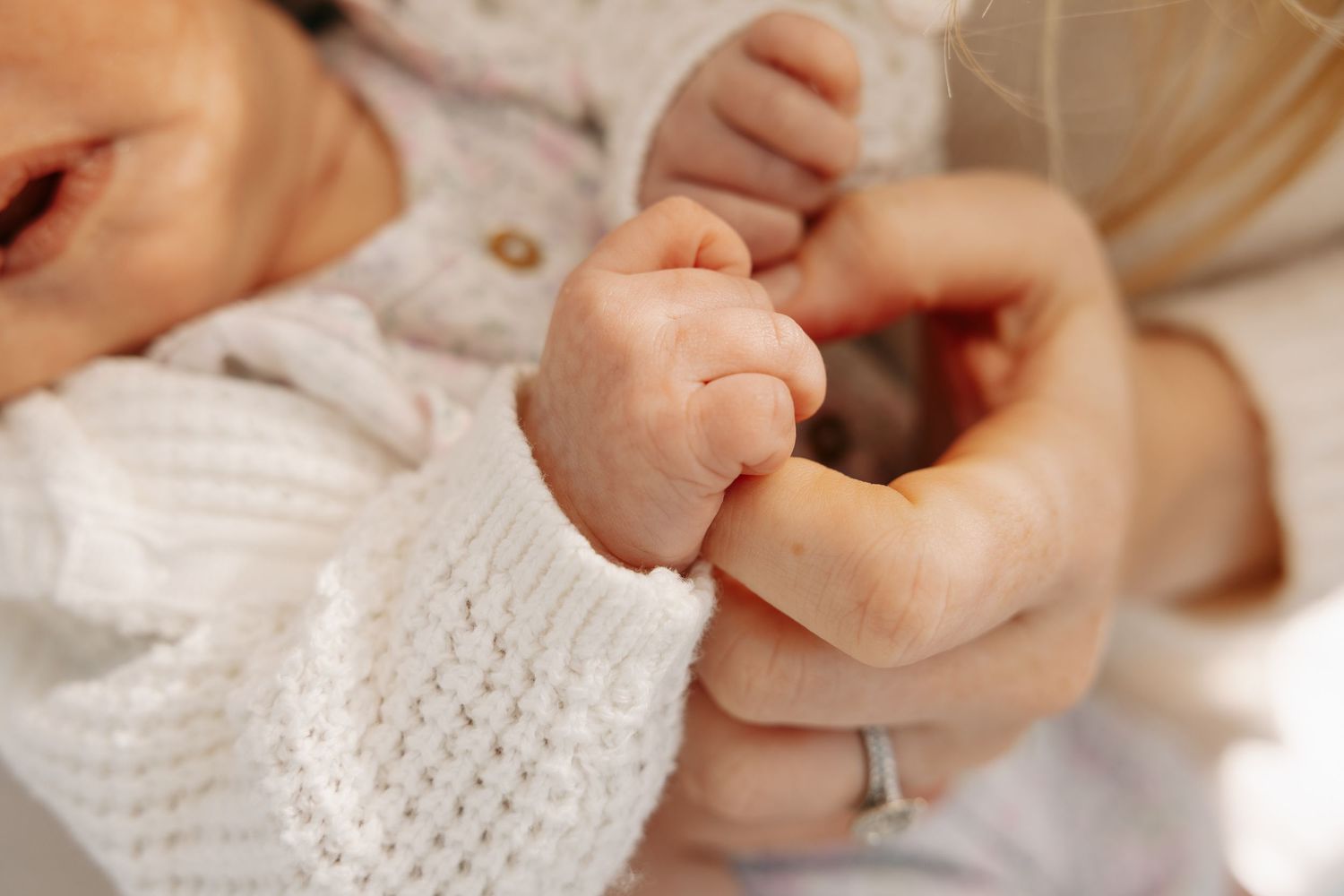 Newborn baby grasping adult finger, close-up of tiny infant hand holding parent's finger, bonding moment.