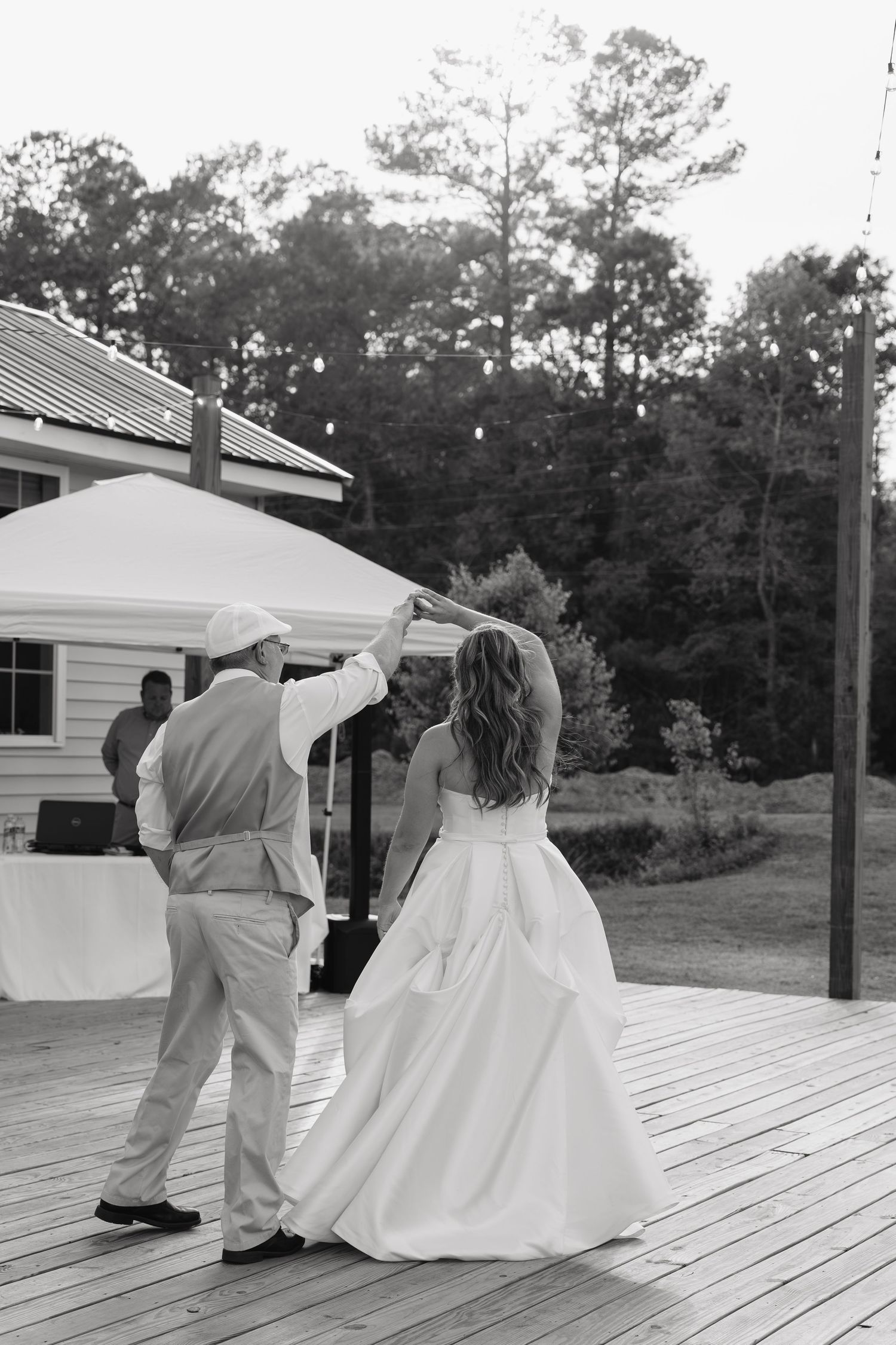 Black and white photo of bride and groom sharing first dance on outdoor deck at wedding reception.