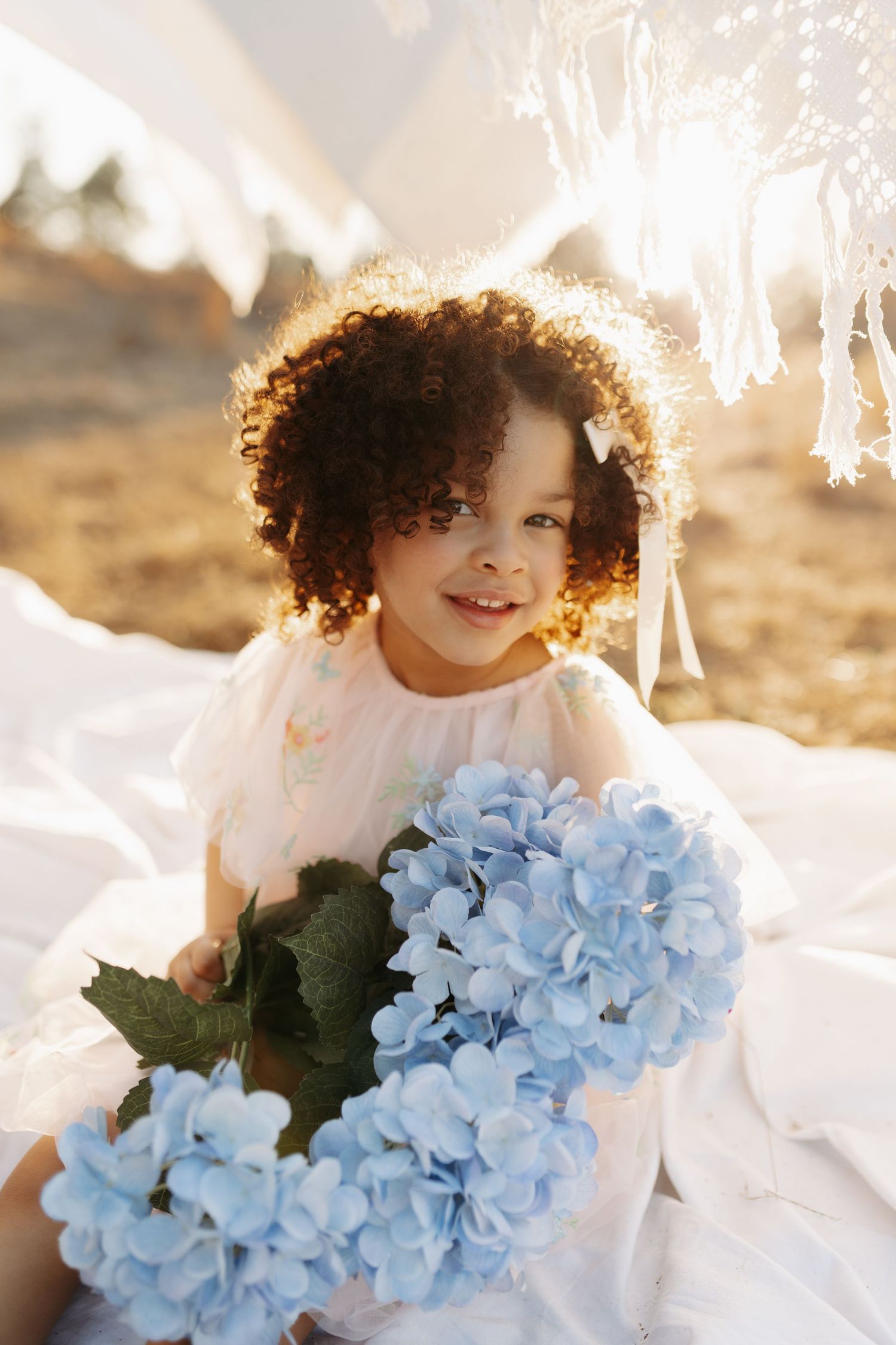 A person in white holds a bouquet of light blue hydrangea flowers in warm sunlit outdoor setting.