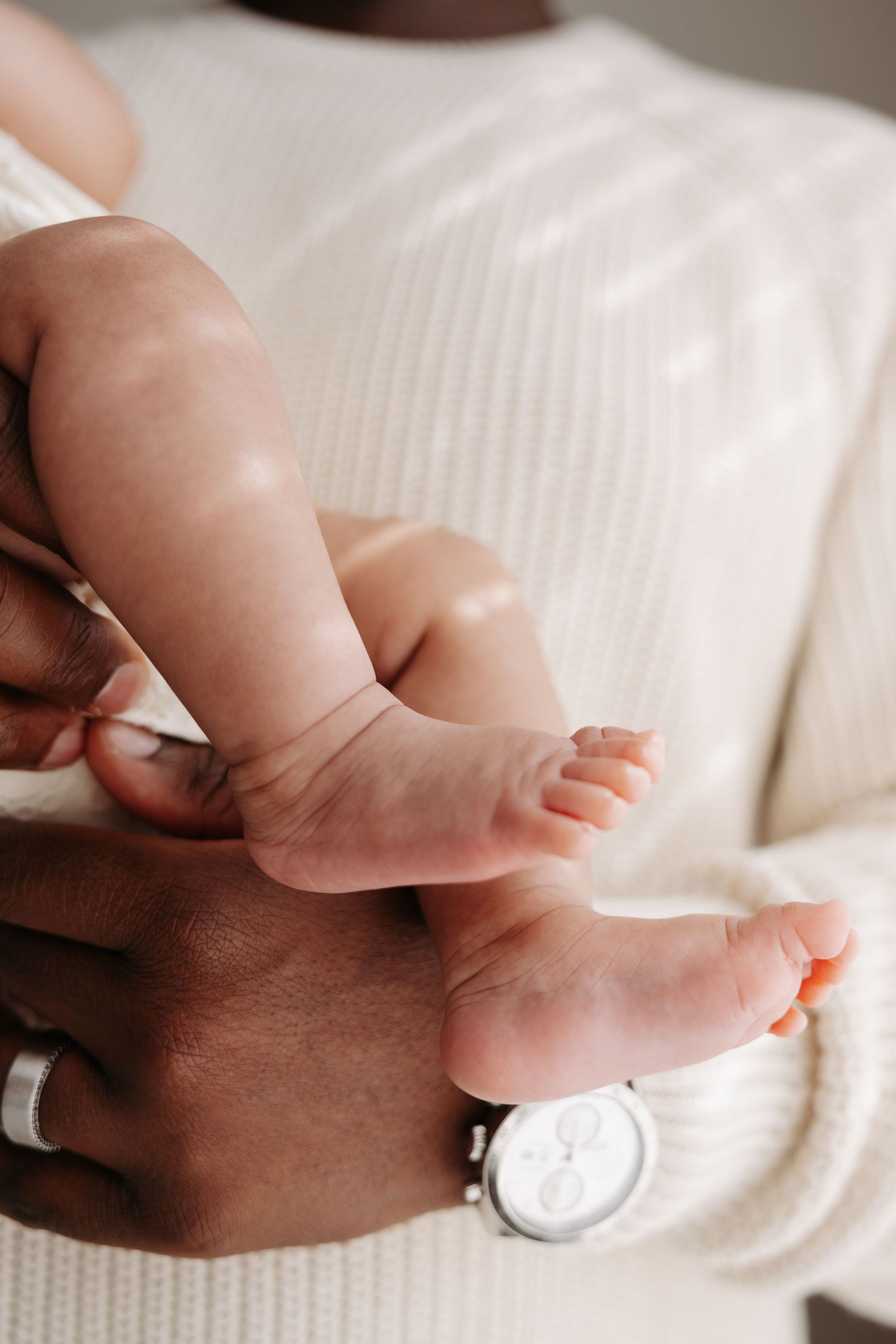 Close-up of a parent's hands gently holding a newborn baby's tiny feet, with a white watch visible on the wrist.