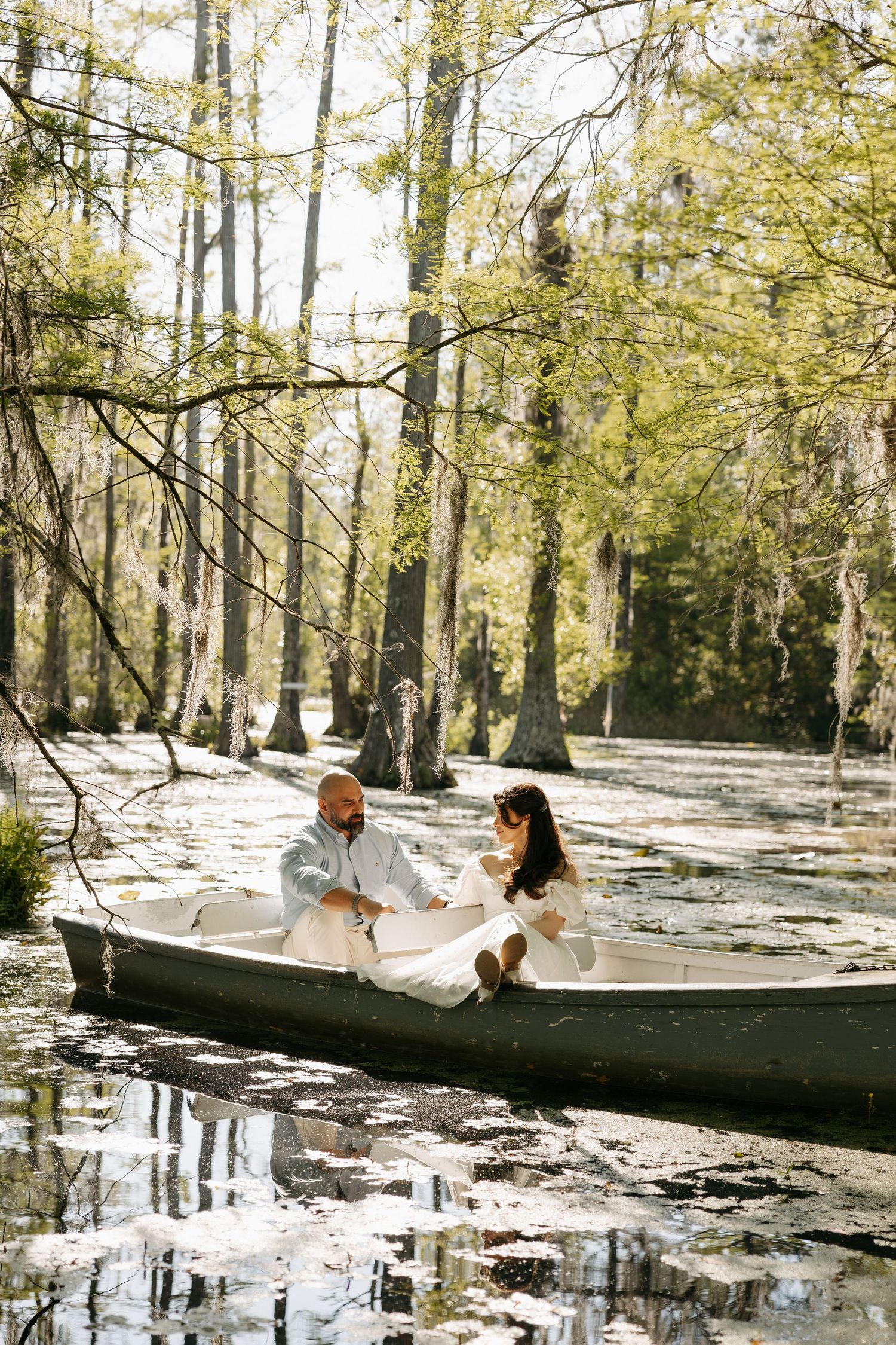Couple in wedding attire sitting in a canoe surrounded by cypress trees in a serene swamp setting.