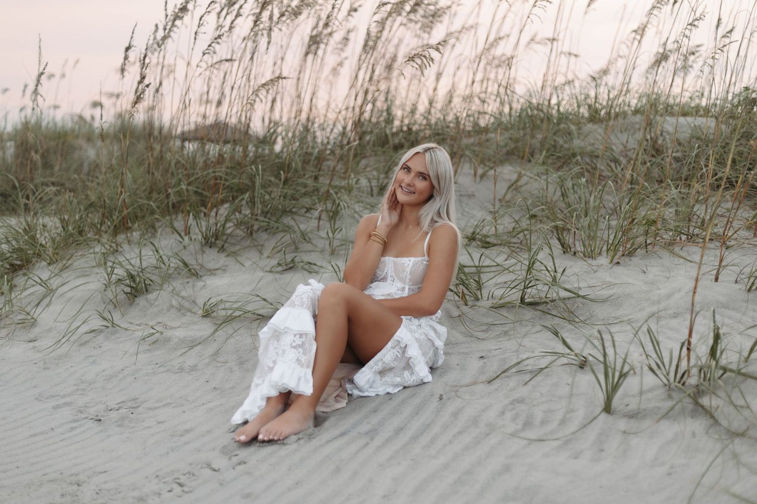 Serene beach scene with beach grass and sand dunes at sunset with figure in white swimwear lounging on sandy shore.