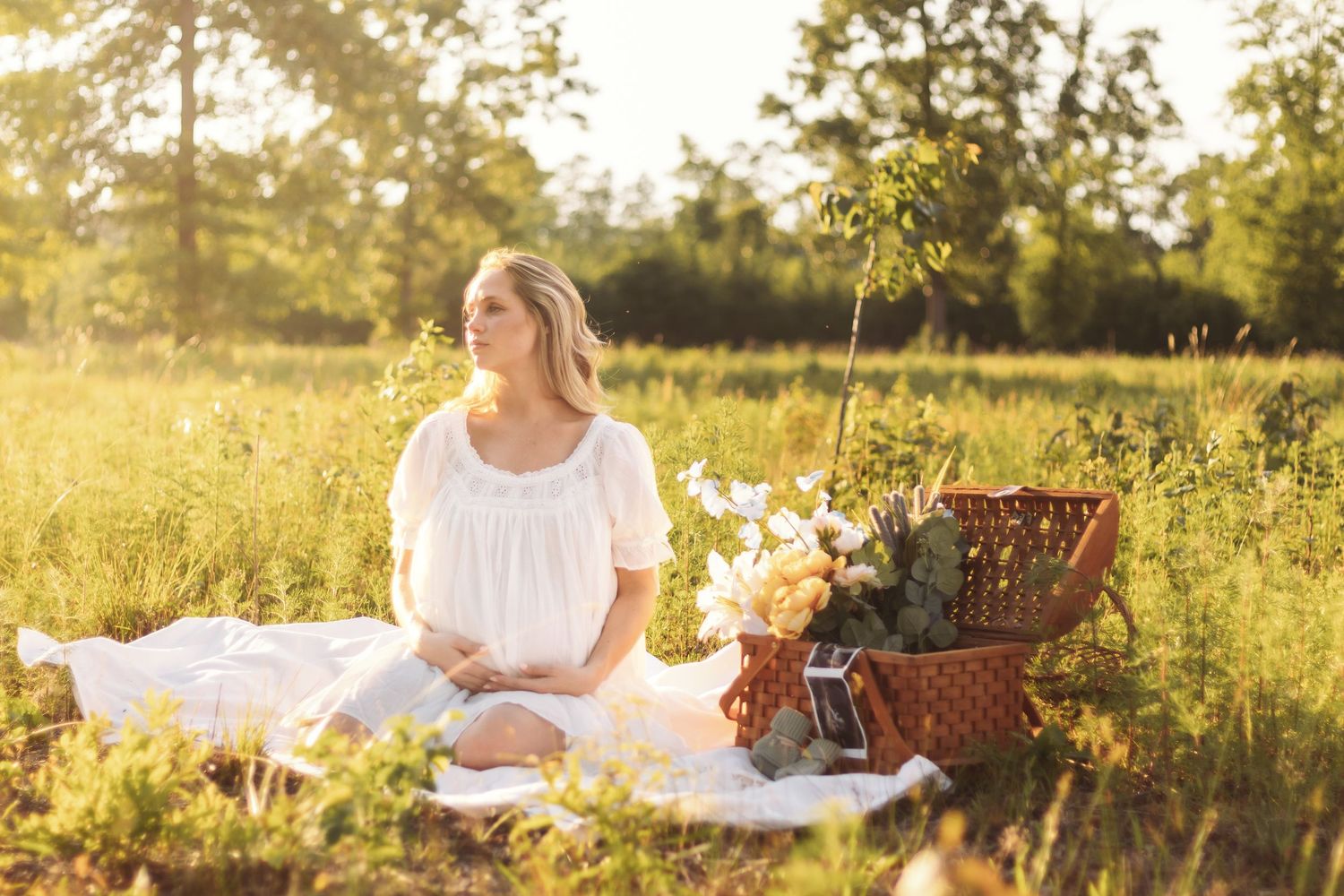 Picnic scene with white blanket and wicker basket in sunlit meadow.