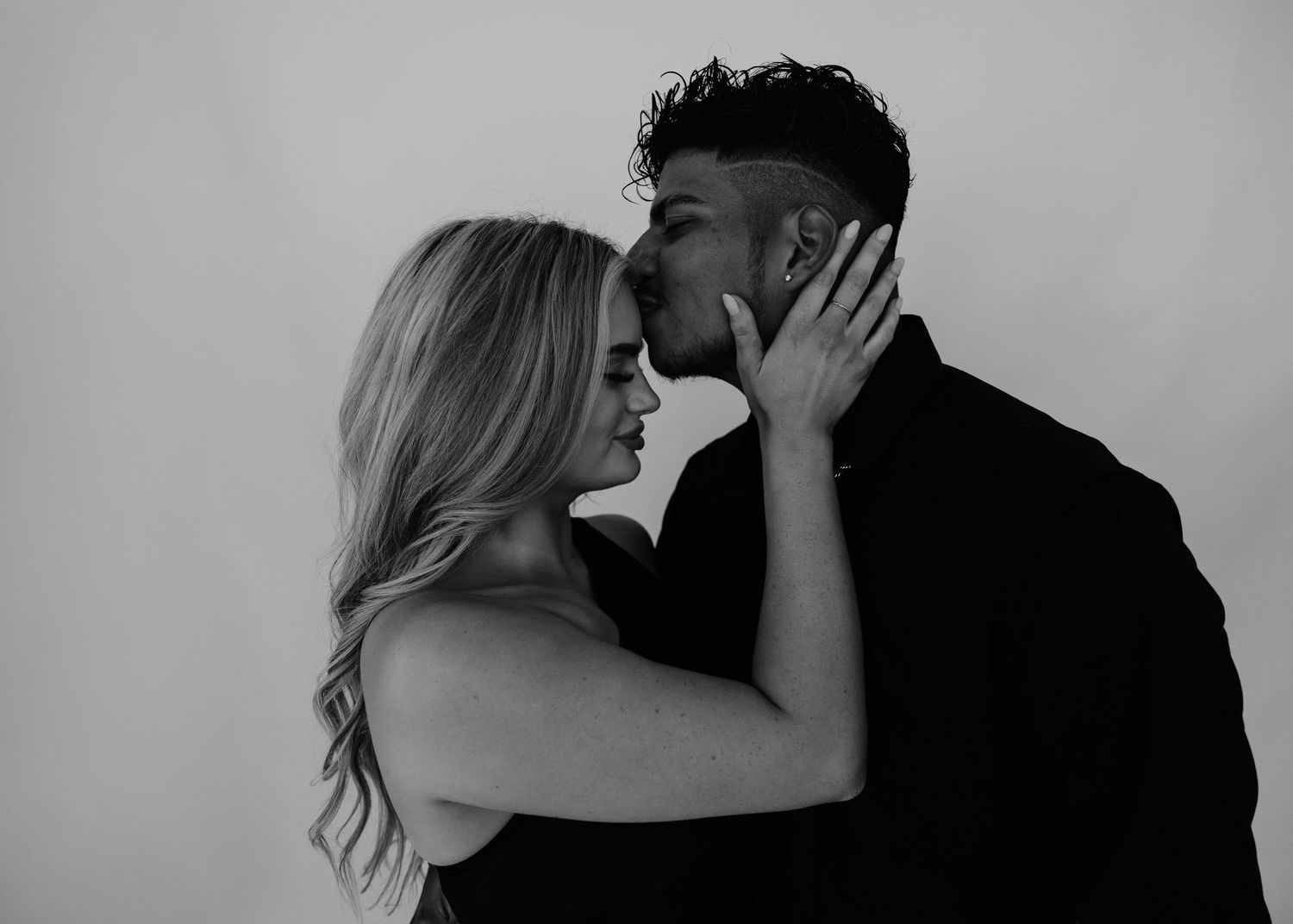 Black and white photo of a romantic couple sharing an intimate moment, woman smiling as man leans in for a kiss.
