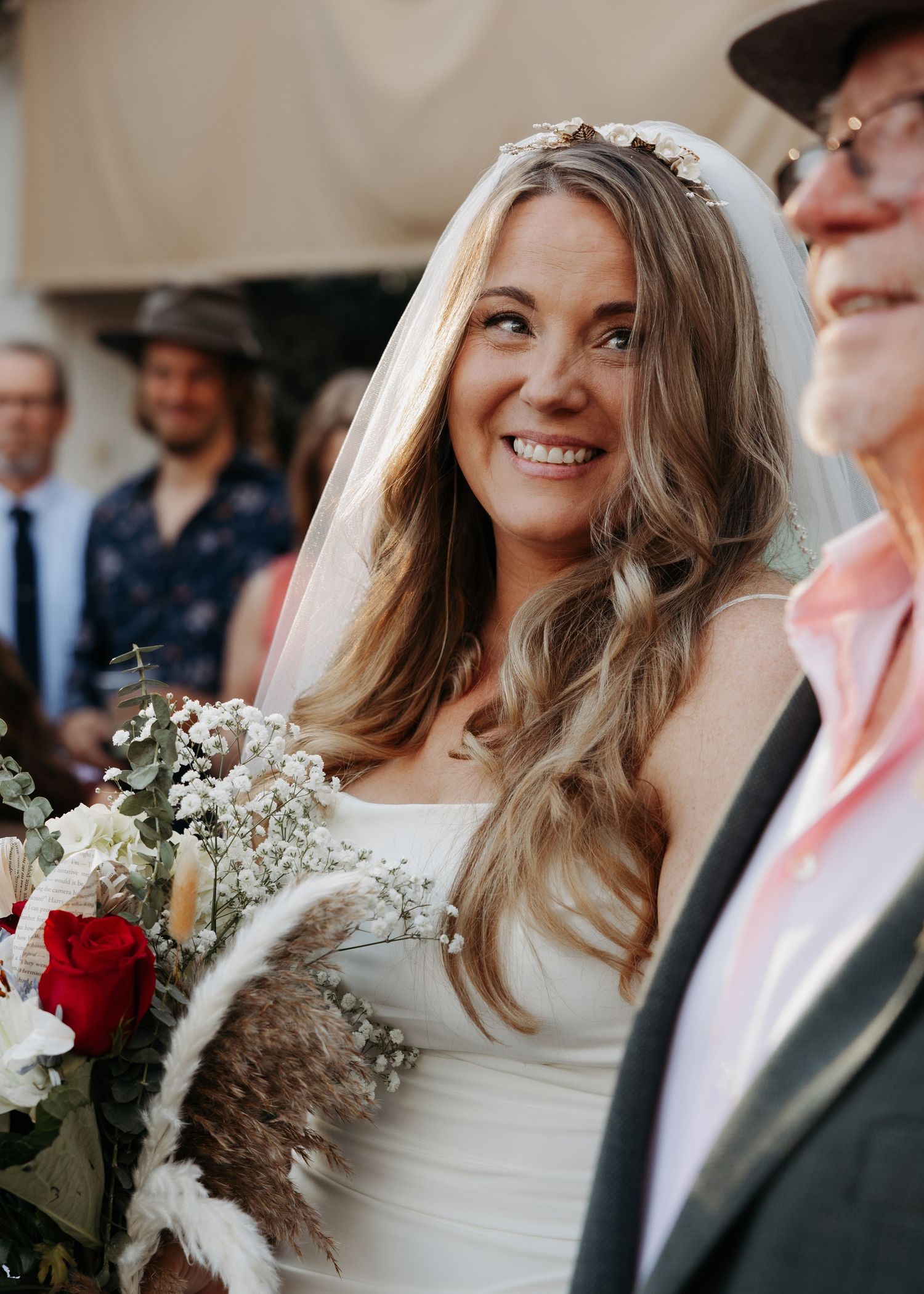 Radiant bride in white gown with floral veil holds bouquet of red and white flowers.