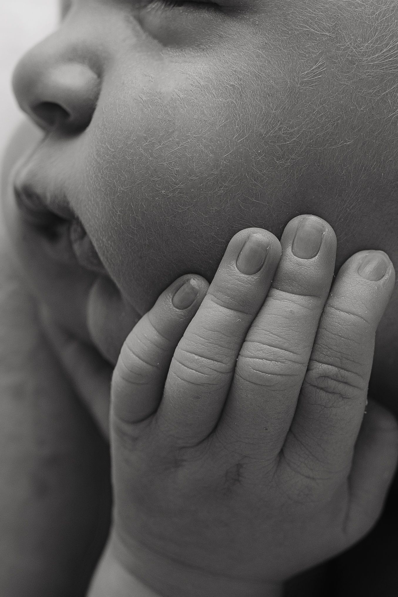 Black and white close-up of a child resting their chin on their hand, showcasing delicate skin texture and fingernails.