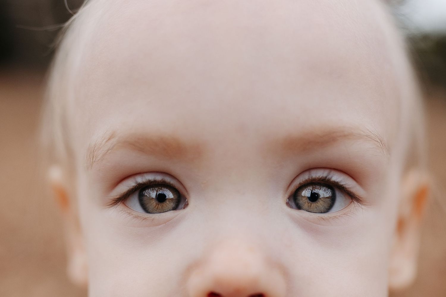 Close up photo of bright brown eyes and rosy cheeks against a blurred outdoor background.