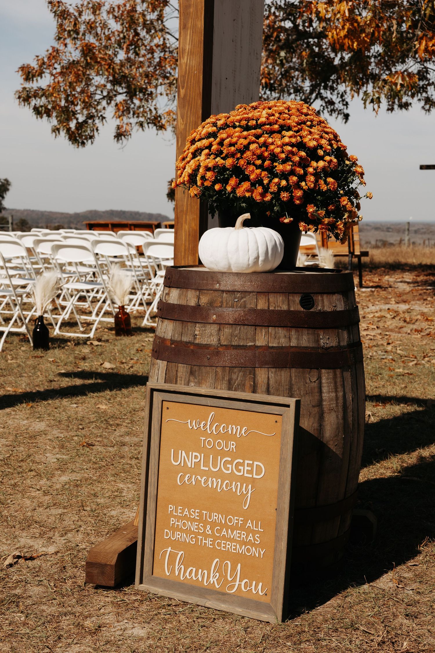 Rustic fall wedding unplugged ceremony sign on wine barrel with orange mums and white pumpkin.
