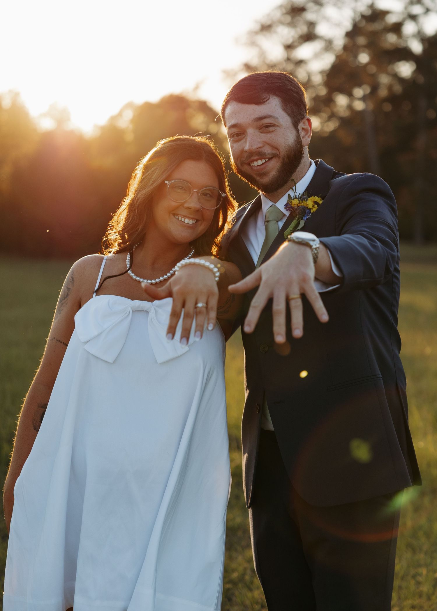 Newlyweds smile and show off wedding rings at golden hour outdoor photo session.