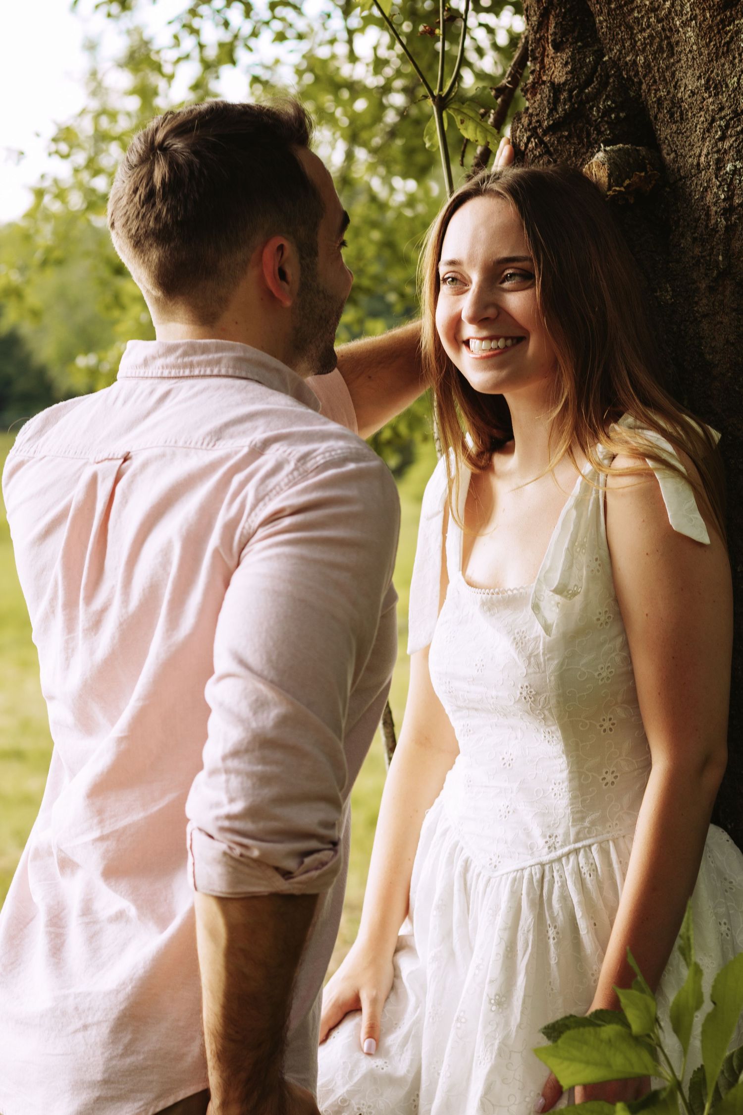 A romantic couple in white outfits sharing a tender moment outdoors in natural sunlight.