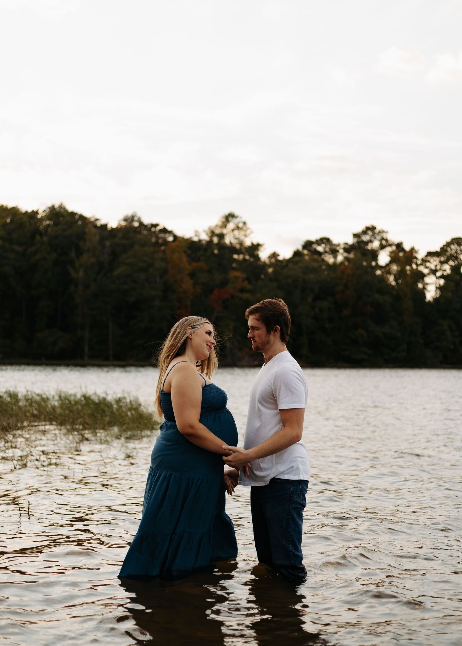 A couple embraces while standing in a lake at sunset, creating a romantic silhouette against the water.