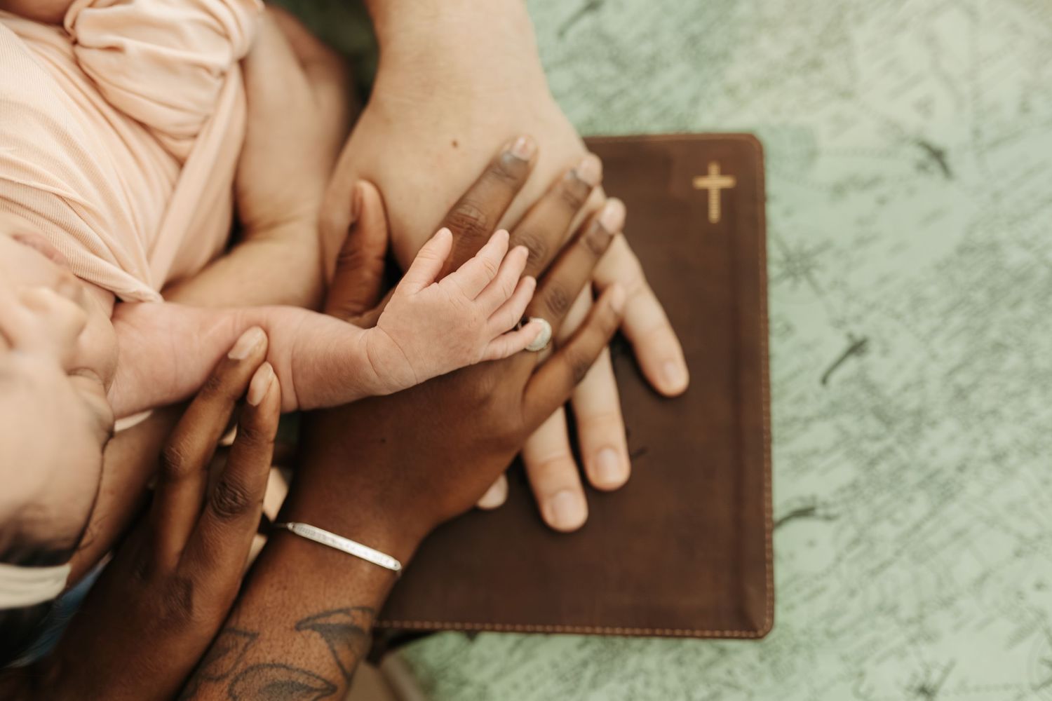 Hands joined in prayer over a brown leather Bible with cross symbol on textured green background.