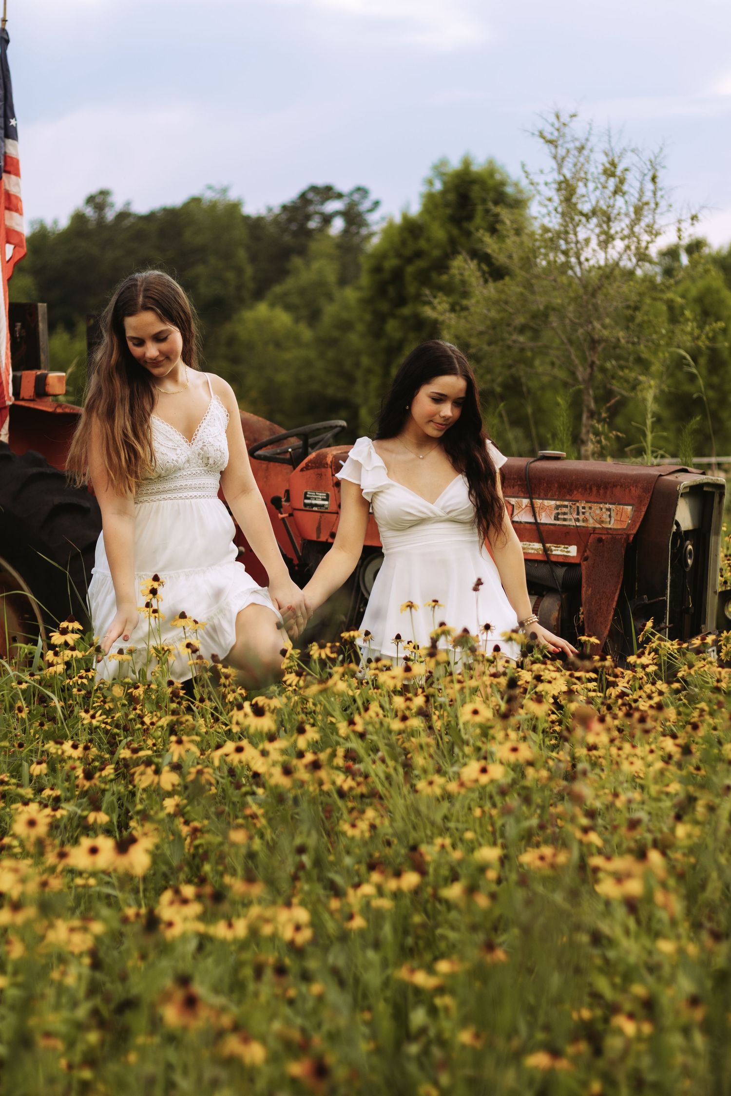 Woman in white dress sits among yellow wildflowers in a rustic field setting during summer.