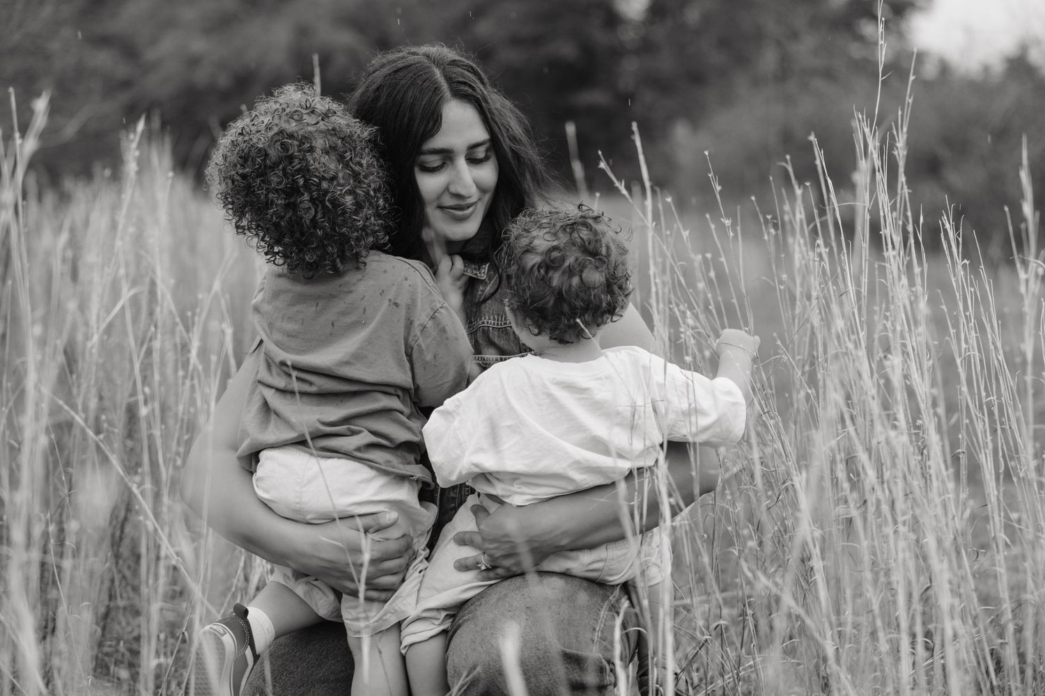 Black and white photo of a mother holding two young children in a field of tall grass.