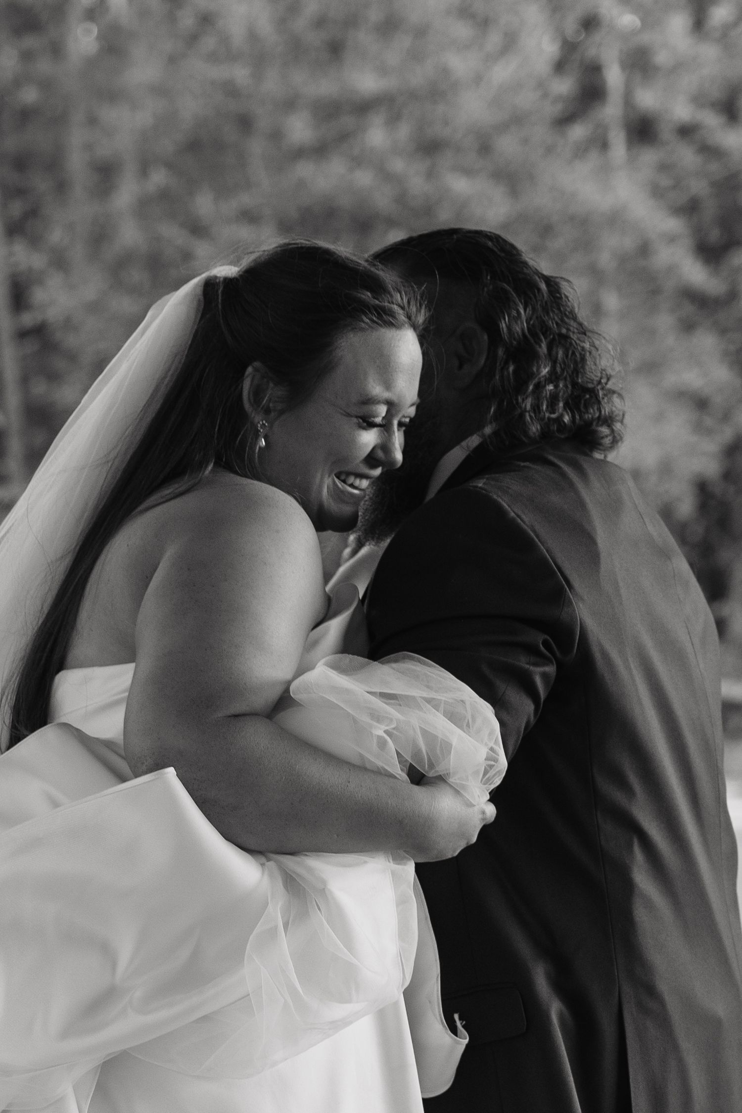 Black and white photo of bride laughing joyfully while embracing groom during emotional first look.