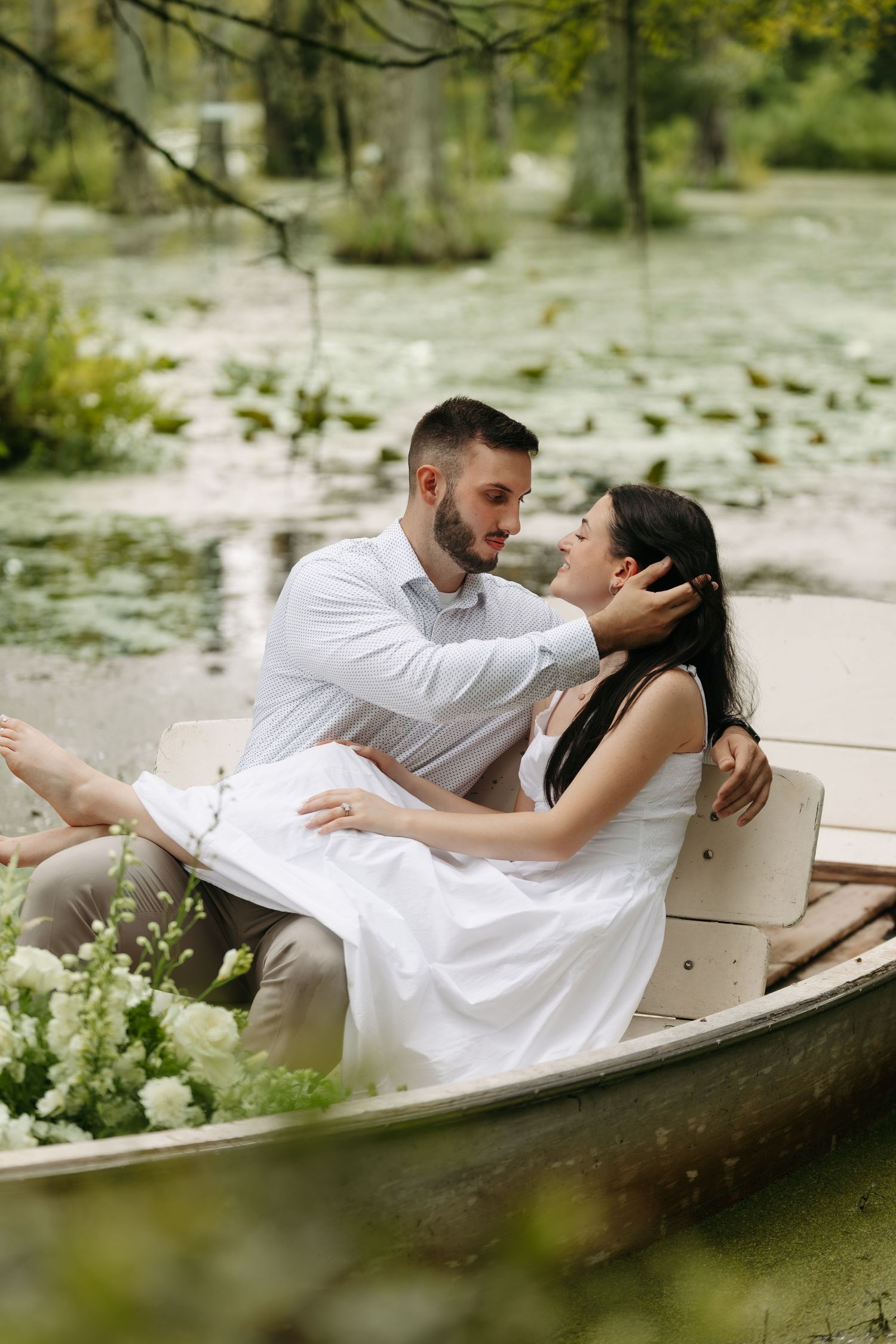 Romantic couple sharing an intimate moment in a flower-adorned rowboat on a serene lily pad lake.