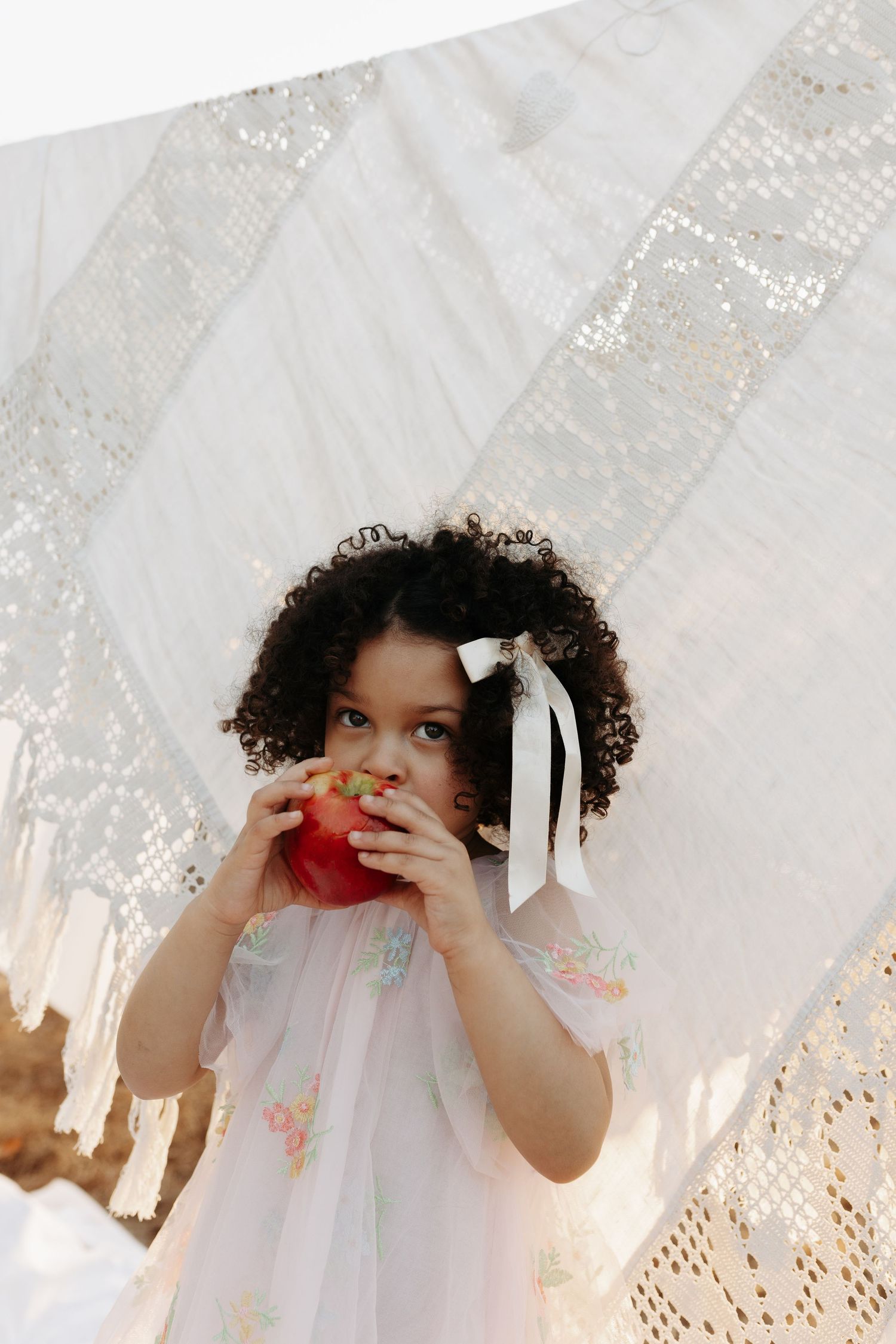A series of photos showing a child in a white dress peeking through lace curtains with natural light streaming in.