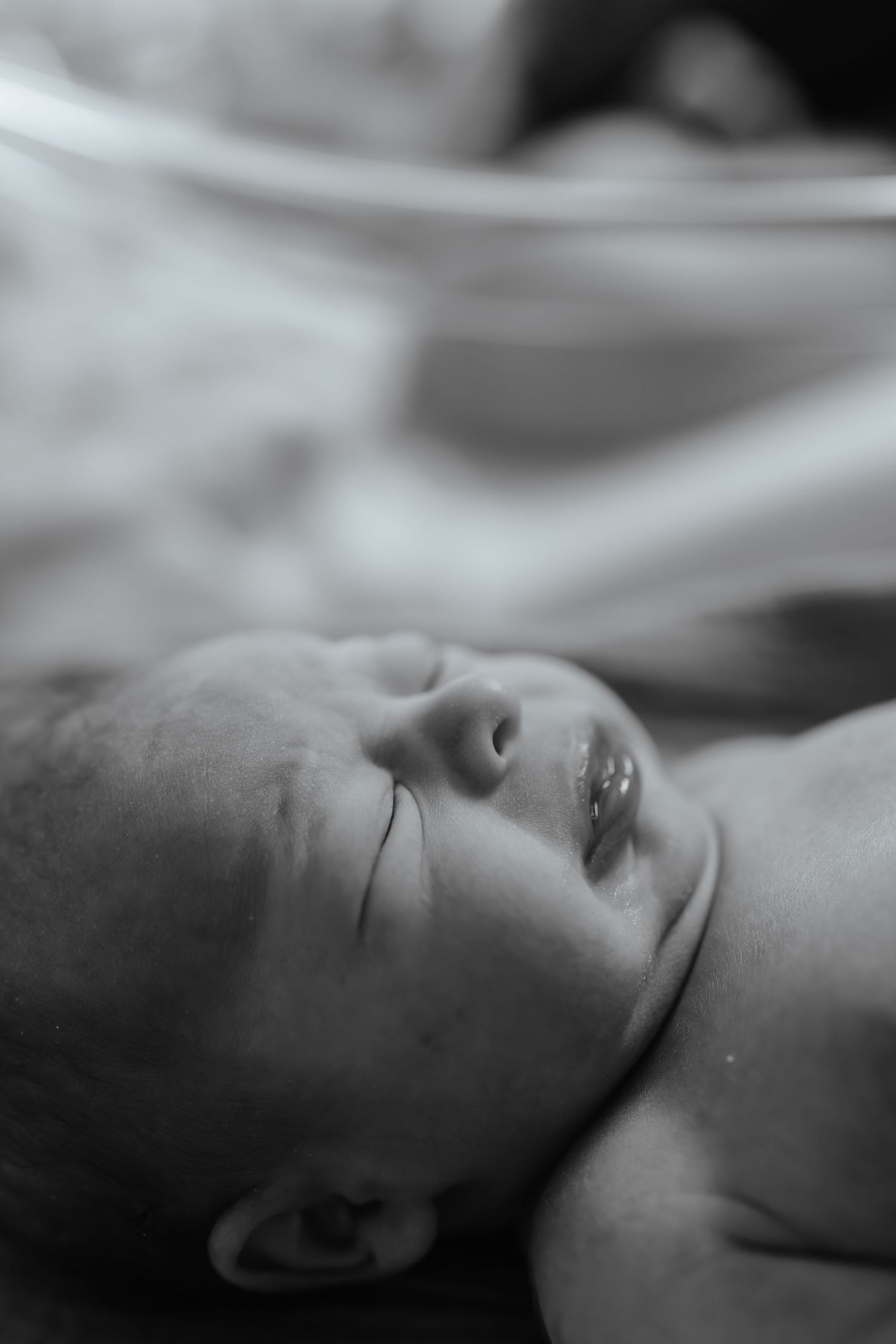 Black and white close-up photo of a sleeping newborn baby lying on a soft white surface.