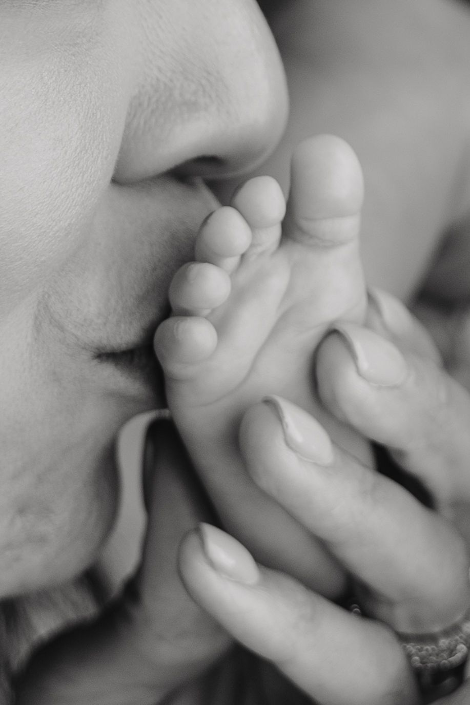 Black and white close-up of a parent kissing a newborn baby's tiny feet, a tender moment of love.