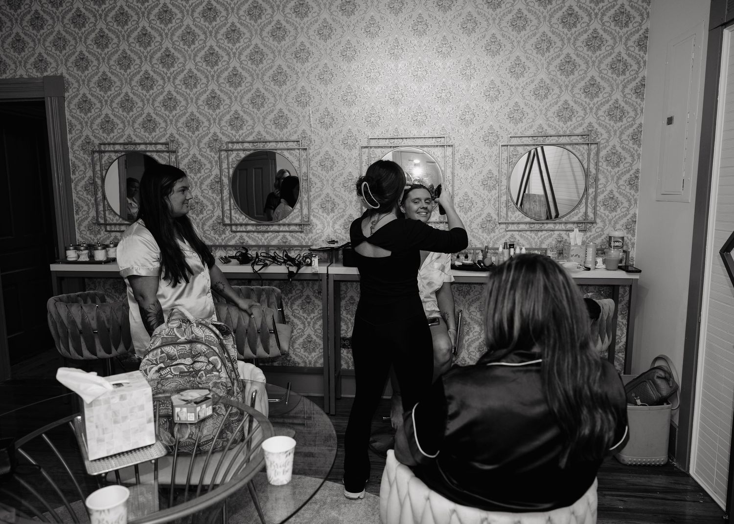 Black and white photo of bridesmaids getting hair and makeup done before a wedding ceremony.