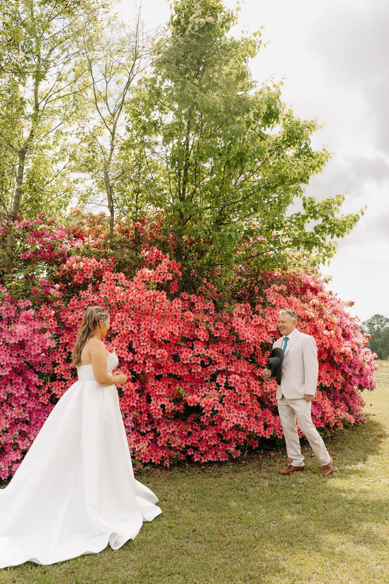 Bride and groom share a first look moment in front of a stunning wall of vibrant pink azalea blooms outdoors.