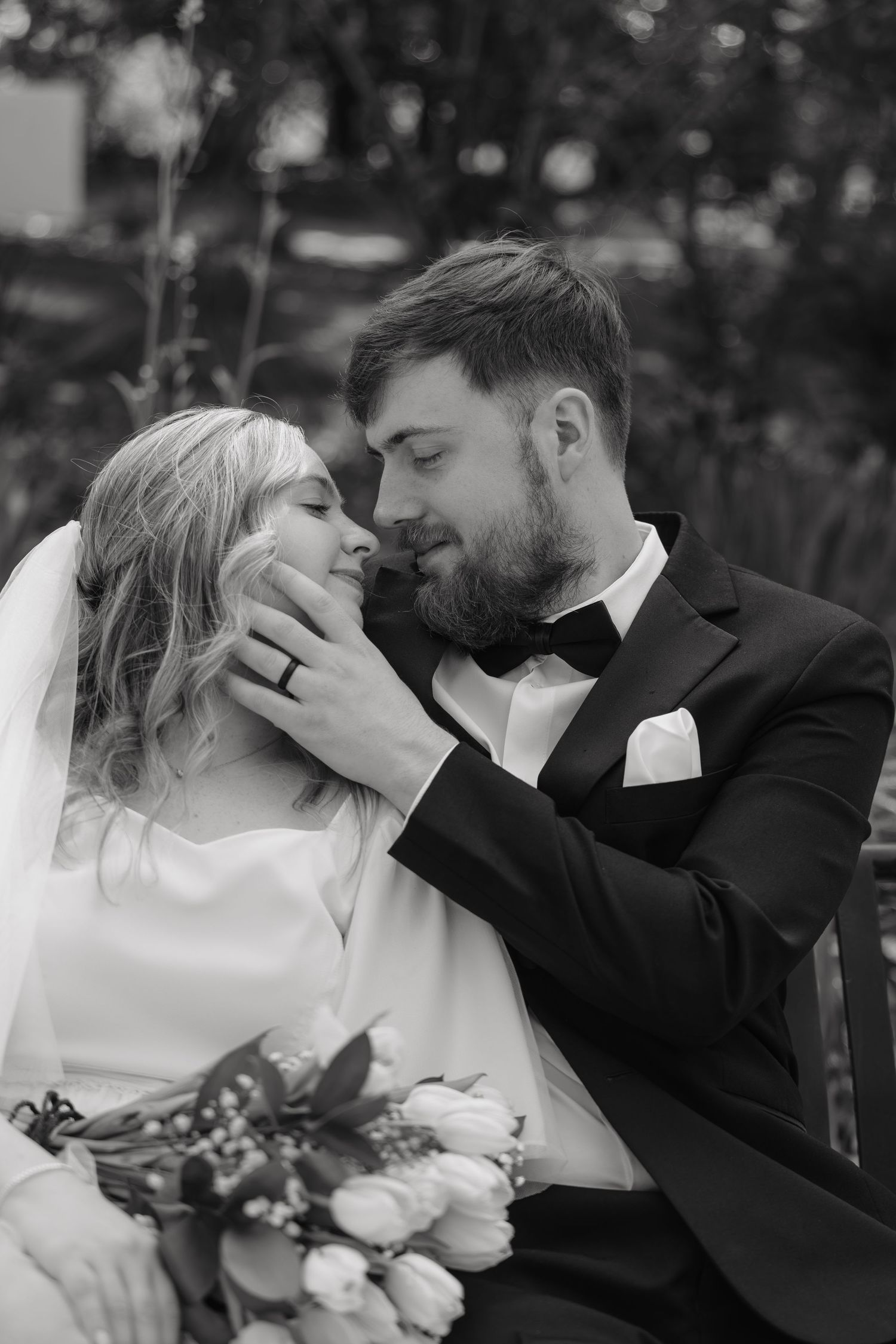 Black and white close-up of groom tenderly cupping brides face with bouquet.