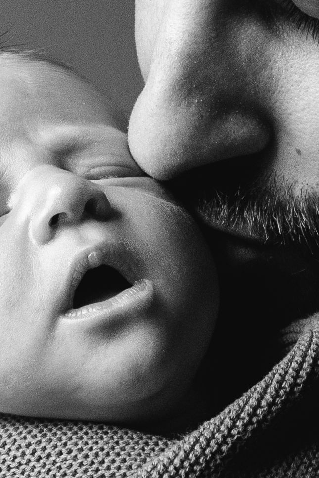 Close-up black and white photograph showing an intimate moment between a person with facial hair and a baby.