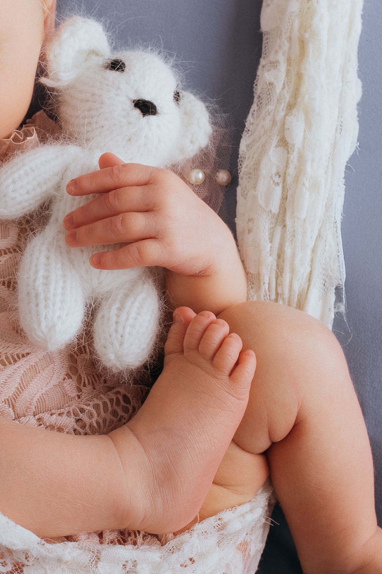 Small baby feet and hands reach out to touch a soft white stuffed bunny toy against a light background.