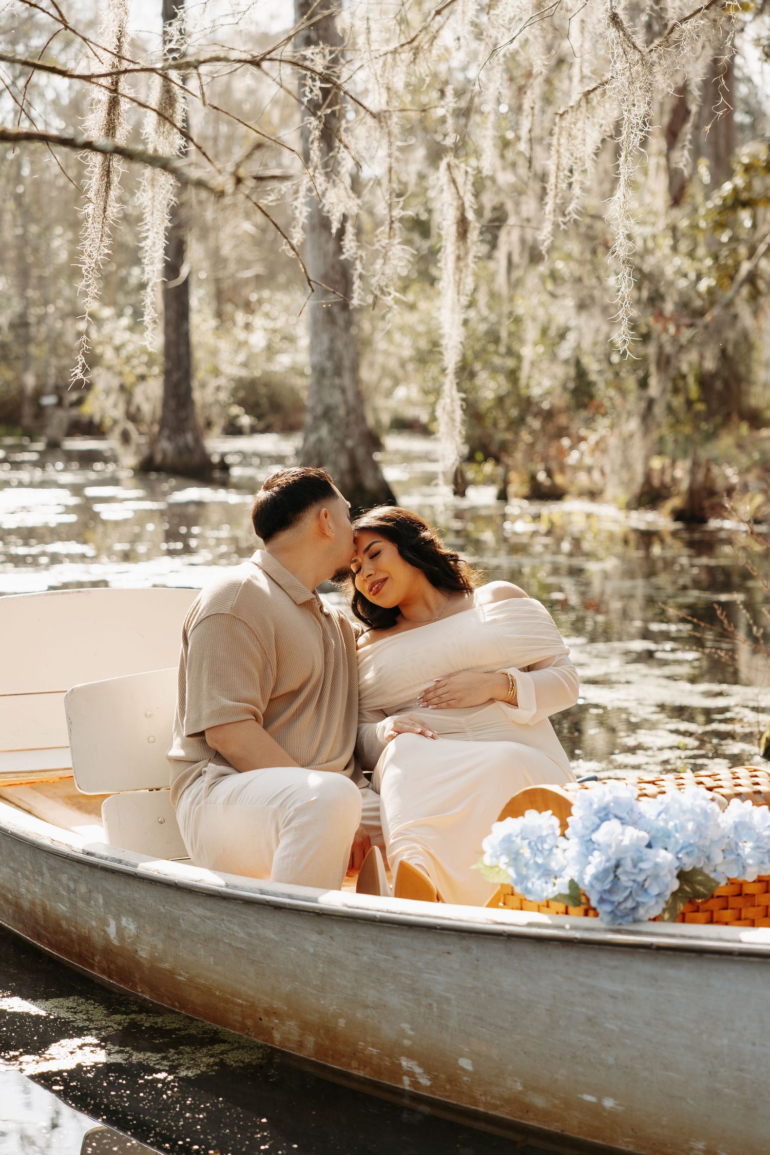 A couple shares a romantic moment in a white boat surrounded by cypress trees draped in Spanish moss on a serene swamp.