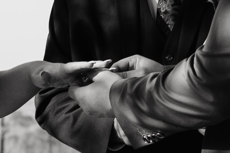 Black and white photo of a groom placing a wedding ring on the bride's finger during a ceremony.