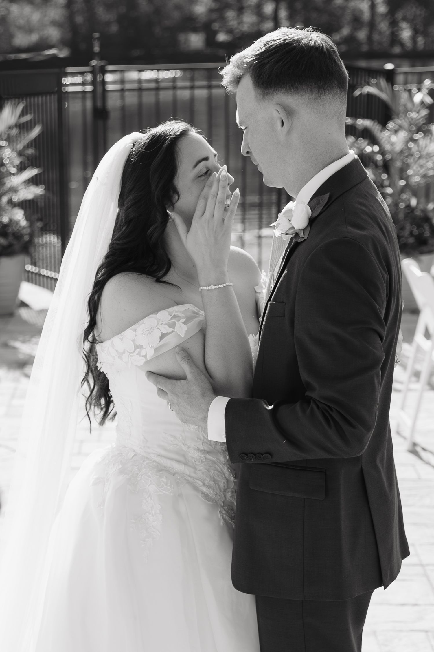 Emotional black and white photo of bride wiping tears while groom tenderly holds her hands at wedding ceremony.
