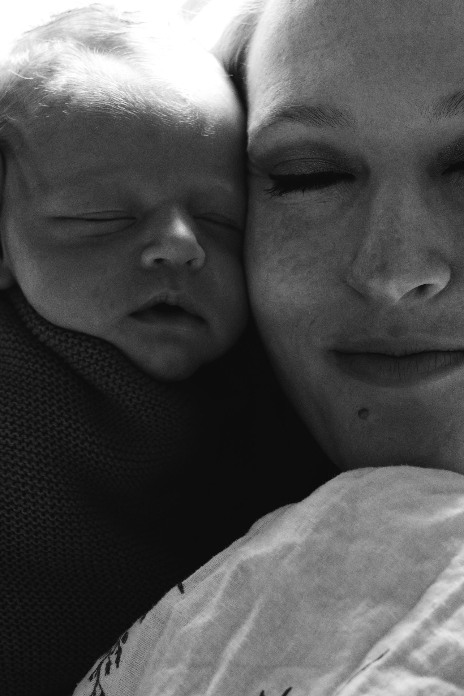 A tender black and white close-up photo of a sleeping infant nestled against someone's face.